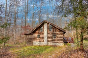 Un chalet rustique en rondins de bois, doté d’une terrasse en bois et d’un porche abrité, entouré d’arbres et d’une zone herbeuse.