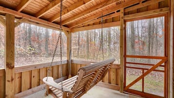 A wooden cabin with a swing chair, large windows, and a view of a forest.