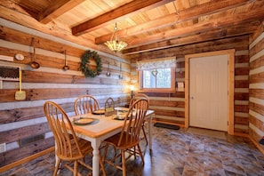 A wooden cabin interior with a dining table, chairs, a chandelier, and a door.