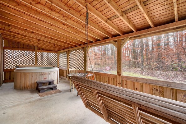 A wooden deck with a hot tub, benches, and a view of a forest. - Navajo in Hocking Hills (Logan)