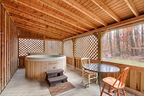 A wooden deck with a hot tub, a table, and chairs.