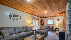 A cozy living room with a wooden ceiling, a gray sofa, a wooden coffee table, and a stone wall. - Navajo in Hocking Hills (Logan)