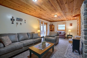 A cozy living room with a wooden ceiling, a gray sofa, a wooden coffee table, and a stone wall. - Navajo in Hocking Hills (Logan)