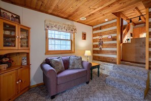 A cozy room with a wooden ceiling, a purple sofa, a wooden cabinet, and a window with a floral curtain. - Navajo in Hocking Hills (Logan)