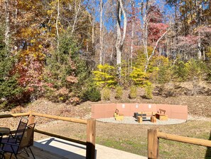 A deck with a table and chairs, surrounded by a wooden railing, overlooking a forested area with autumn foliage. - Dewdrop Inn in Hocking Hills (Logan)