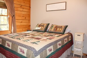 A bedroom with a wooden headboard, a quilted bedspread, two decorative pillows, a framed sign on the wall, and a small white cabinet. - Dewdrop Inn in Hocking Hills (Logan)