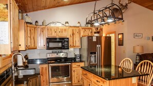 A kitchen with wooden cabinets, stainless steel appliances, a black countertop, and a chandelier. - Dewdrop Inn in Hocking Hills (Logan)