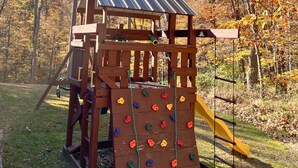 A wooden play structure with a slide and climbing wall in a park.