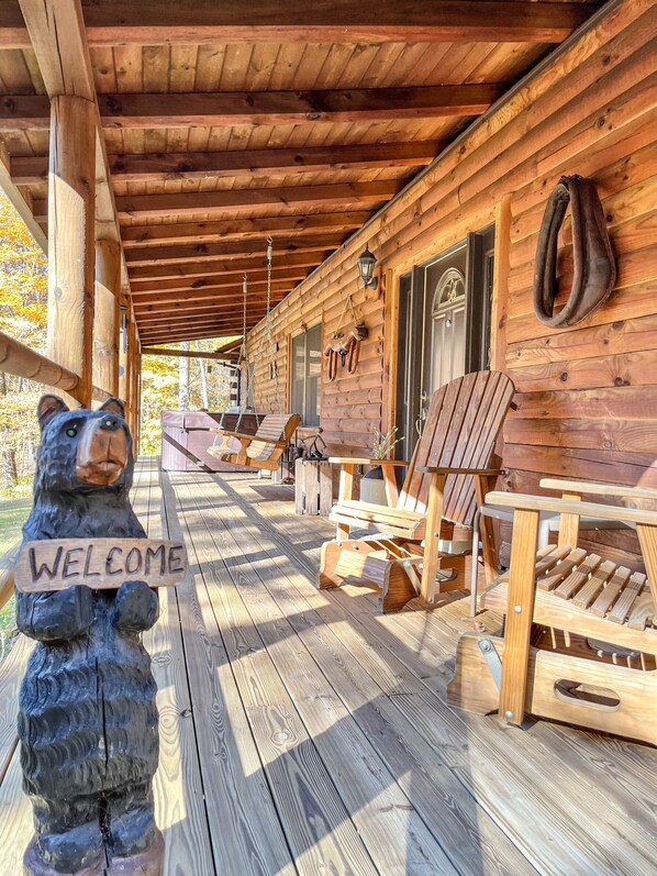A wooden cabin with a porch, outdoor seating, and a bear statue holding a welcome sign.