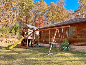 A wooden cabin with a swing set and a slide in a wooded area.