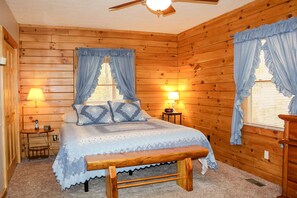 A cozy wooden cabin bedroom with a bed, two bedside tables with lamps, a bench, and a ceiling fan. - Dewdrop Inn in Hocking Hills (Logan)