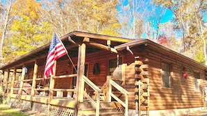 A wooden log cabin with a porch and a flag. - Dewdrop Inn in Hocking Hills (Logan)