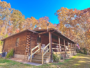 A wooden cabin with a porch and steps, surrounded by trees with autumn foliage.
