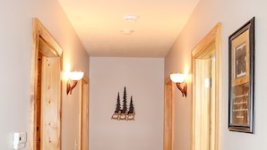 A hallway with wooden doors, a small table with decorative birds, and a wall-mounted light fixture. - Dewdrop Inn in Hocking Hills (Logan)