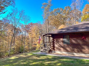 A rustic cabin with a wooden exterior, a porch, and a flag. - Dewdrop Inn in Hocking Hills (Logan)