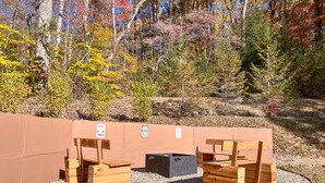 A wooden bench area with a gravel path, surrounded by a low wall and autumn foliage.