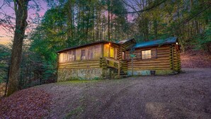 Une cabane rustique en rondins de bois, avec des fondations en pierre, une terrasse en bois et un porche.