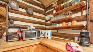 Une cuisine avec des meubles de rangement en bois, un four à micro-ondes, un grille-pain, une machine à café et des étagères où sont rangés de la verrerie et des tasses.