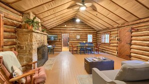 L’intérieur d’une cabane en rondins, avec une cheminée en pierre, des meubles en bois et un coin repas.