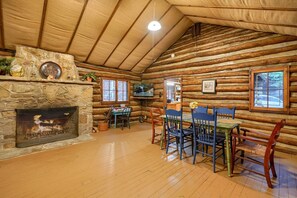 A log cabin interior with a stone fireplace, wooden dining table, and chairs. - Russell Cabin in Hocking Hills (South Bloomingville)