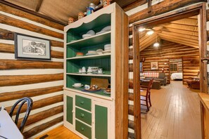 A cozy log cabin interior with a dining area, a green cabinet with dishes, and a framed picture on the wall.