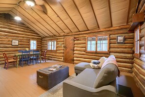A log cabin interior with a dining area, sofa, and a large window. - Russell Cabin in Hocking Hills (South Bloomingville)