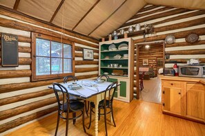 L’intérieur d’un chalet rustique présente une table à manger dressée pour quatre personnes, entourée de murs en bois et surplombée d’un plafond en bois.