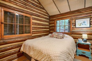 A log cabin bedroom with a large bed, a window, and a nightstand with a lamp.