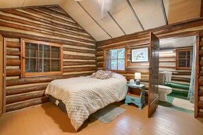 Une chambre dans un chalet en rondins, avec un lit, une table de chevet et une vue sur la salle de bain.