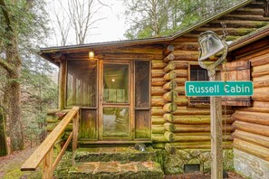 A rustic cabin with a wooden staircase leading to a glass door, surrounded by trees.