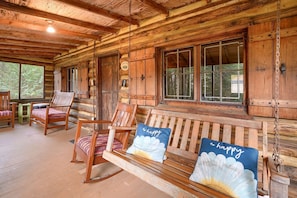 A wooden cabin interior with a wooden bench, rocking chairs, and a table.
