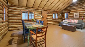 L’intérieur d’une cabane en rondins, avec une table à manger, des chaises, un canapé et une cheminée.