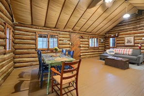 Ein rustikales Blockhaus-Interieur mit Esstisch, Stühlen, einer Couch und einem Kamin.