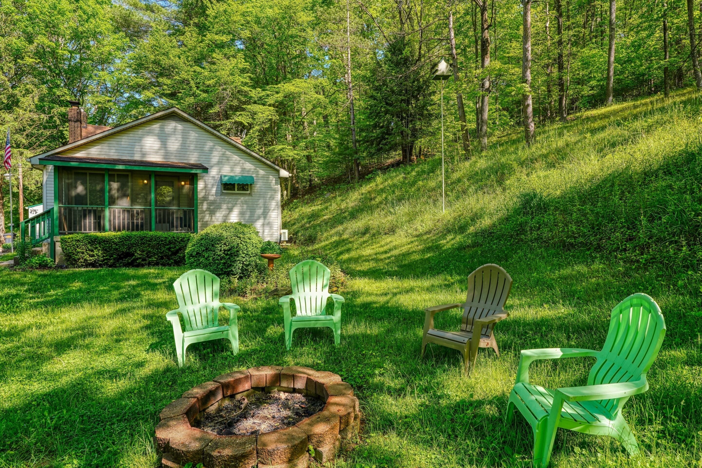 Une cabane dotée d’un porche, entourée d’une pelouse où se trouvent des fauteuils Adirondack et un foyer.