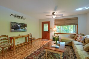 A living room with a wooden floor, a sofa, a coffee table, a fireplace, and a painting on the wall. - Hillside Hideaway in Hocking Hills (Logan)