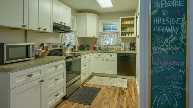 A modern kitchen with white cabinets, a microwave, a toaster, and a chalkboard with a welcome message. - Hillside Hideaway in Hocking Hills (Logan)