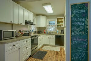 A kitchen with white cabinets, a microwave, a toaster, and a chalkboard with a welcome message.