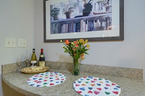 A kitchen counter with a framed picture, two wine bottles, a vase with flowers, and two heart-patterned placemats. - Hillside Hideaway in Hocking Hills (Logan)