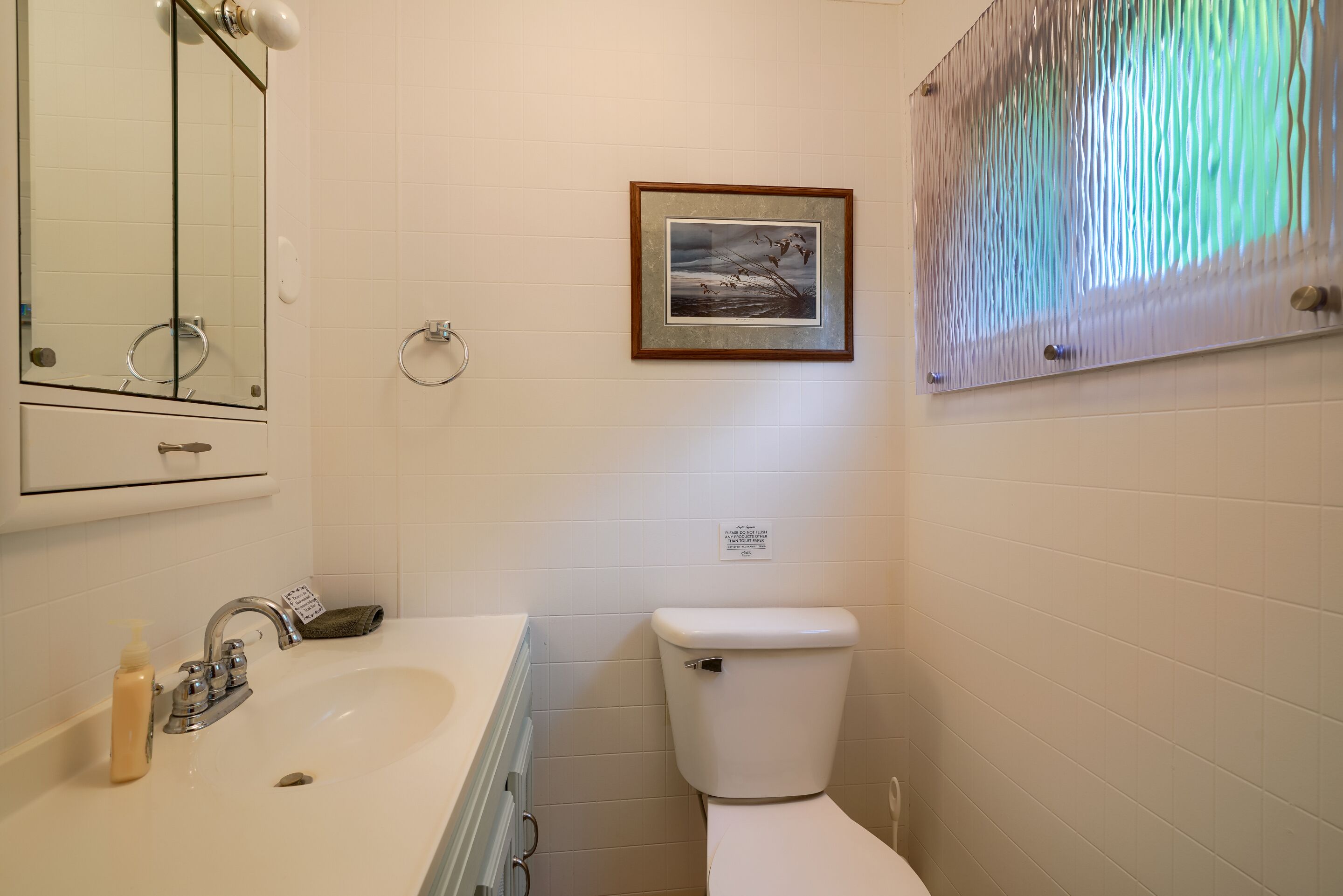 A bathroom with a sink, toilet, and a framed picture on the wall.