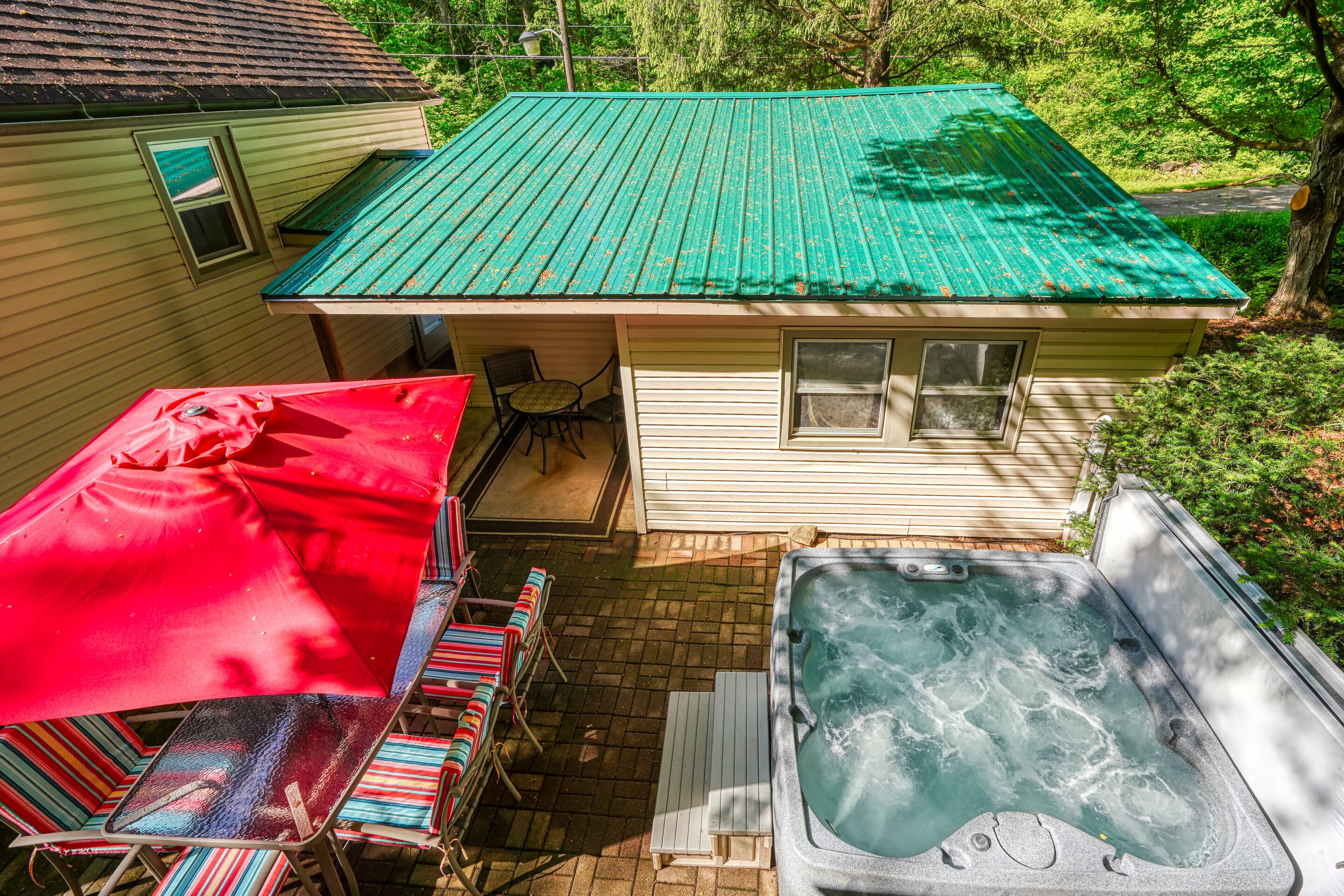 A house with a green roof, a hot tub, and a patio with colorful chairs and a red table.