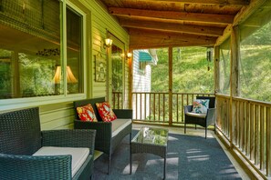 A covered porch with wicker furniture, a glass table, and a view of a green house in the background. - Hillside Hideaway in Hocking Hills (Logan)