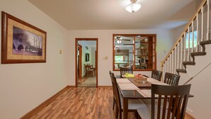 A dining area with a wooden table and chairs, a framed picture on the wall, and a staircase with a railing. - Hillside Hideaway in Hocking Hills (Logan)