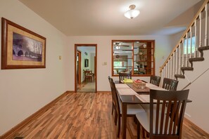 A dining area with a wooden floor, a dining table with chairs, a framed picture on the wall, and a staircase with a railing. - Hillside Hideaway in Hocking Hills (Logan)