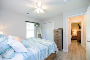 A bedroom with a bed, a dresser, a ceiling fan, and a hallway leading to another room. - Family Friendly Beach Bungalow 2 blocks to beach, minutes from Hampton U & LAFB (Hampton)