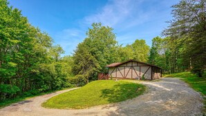 A gravel driveway leading to a building with a sloped roof, surrounded by lush greenery and trees. - Hideaway Pines Cabin (Logan)