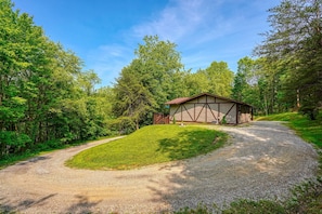 A gravel driveway leading to a building with a sloped roof, surrounded by lush greenery and trees. - Hideaway Pines Cabin (Logan)