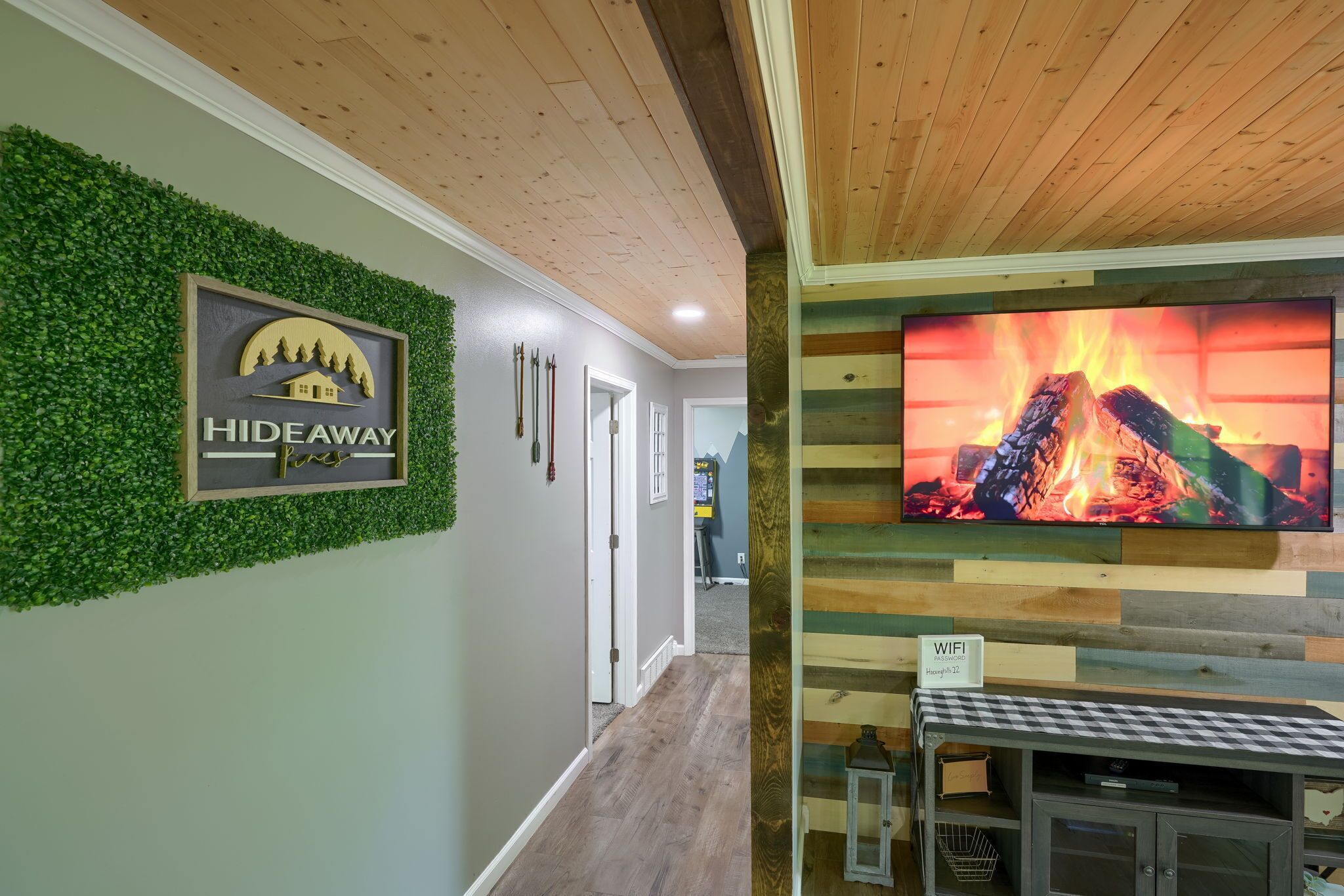 Ein Flur mit einem Schild, das 'HIDEAWAY Pines' zeigt, einer Holzzieldecke, einem Fernseher, der ein Feuer anzeigt, und einem karierten Tisch.