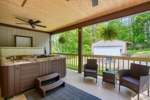 A covered outdoor kitchen area with a built-in stove, a ceiling fan, and a view of a garage and trees. - Hideaway Pines Cabin (Logan)