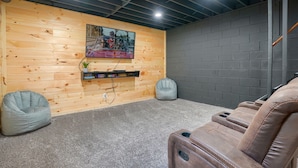A room with a wooden wall, a mounted TV, a grey bean bag chair, and a reclining massage chair. - Hideaway Pines Cabin (Logan)