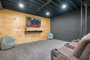 A room with a wooden wall, a mounted TV, a grey bean bag chair, and a reclining massage chair. - Hideaway Pines Cabin (Logan)